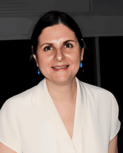 Smiling woman in white top with blue earrings.